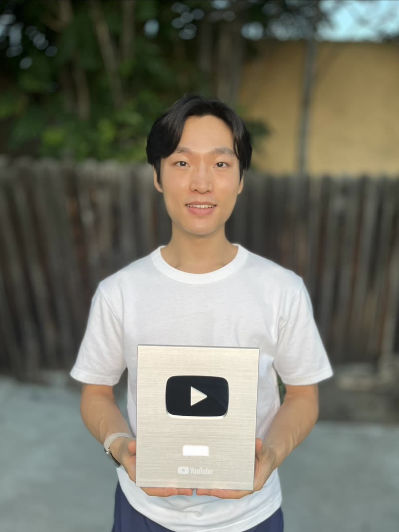 A creator holding a silver YouTube play button award outdoors by a fence
