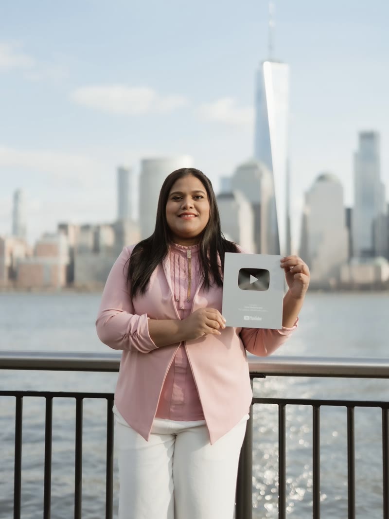 A creator holding a silver YouTube play button award in front of the New York skyline