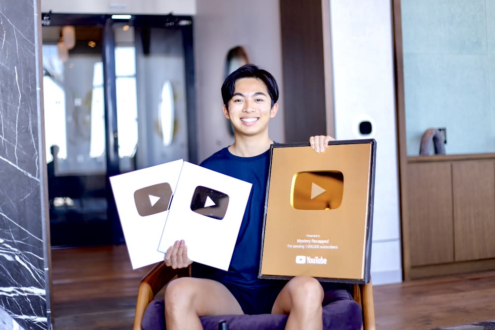 A creator seated holding a gold YouTube play button award alongside two silver awards