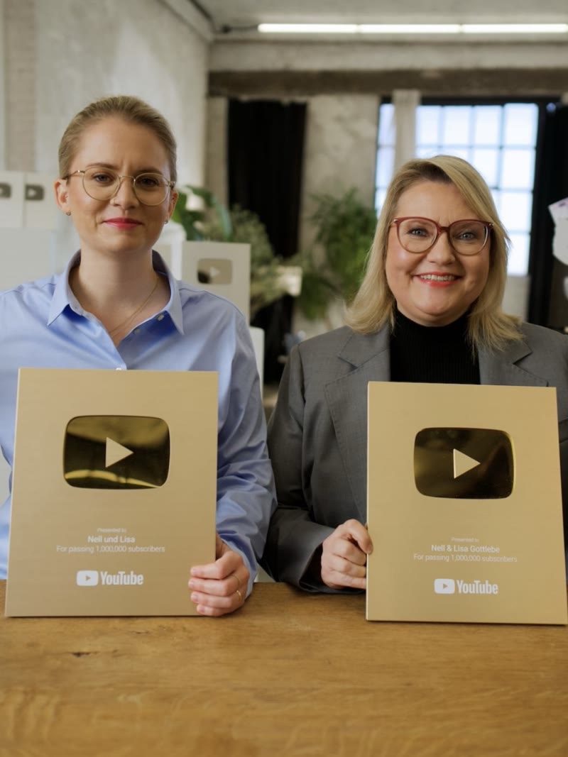 Two creators each holding a gold YouTube play button award at a wooden table